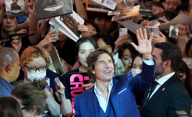 A man in suit waving surrounded by crowds of fans.