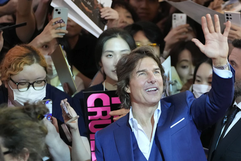 A man in suit waving surrounded by crowds of fans.