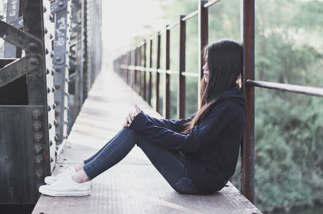 A woman sits on a bridge looking sad.