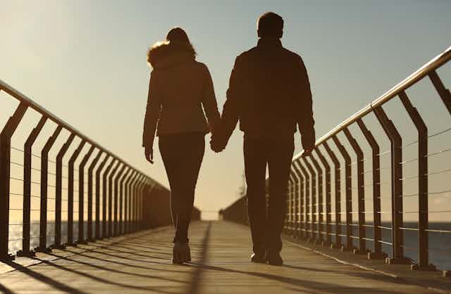 young couple hold hands and walk along bridge