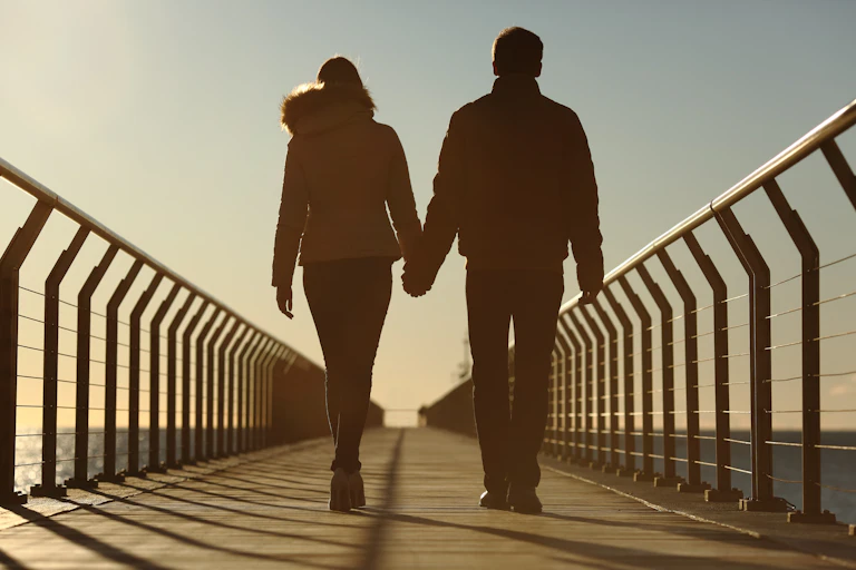 young couple hold hands and walk along bridge