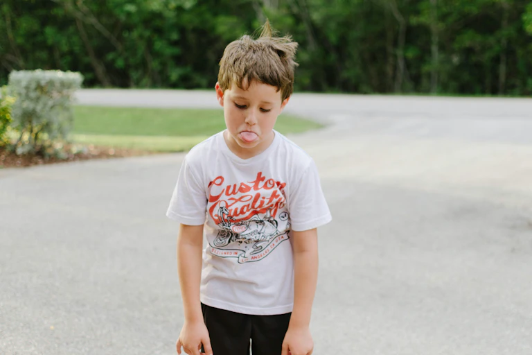 A young boy slumps his shoulder and sticks his tongue out.