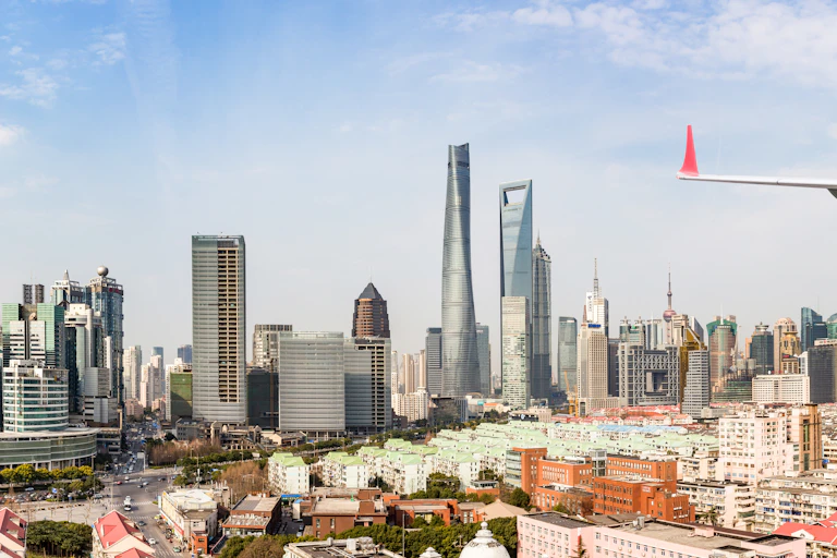 An airplane is shown flying over low-rise residential buildings, with the skyscrapers of Shanghai behind.