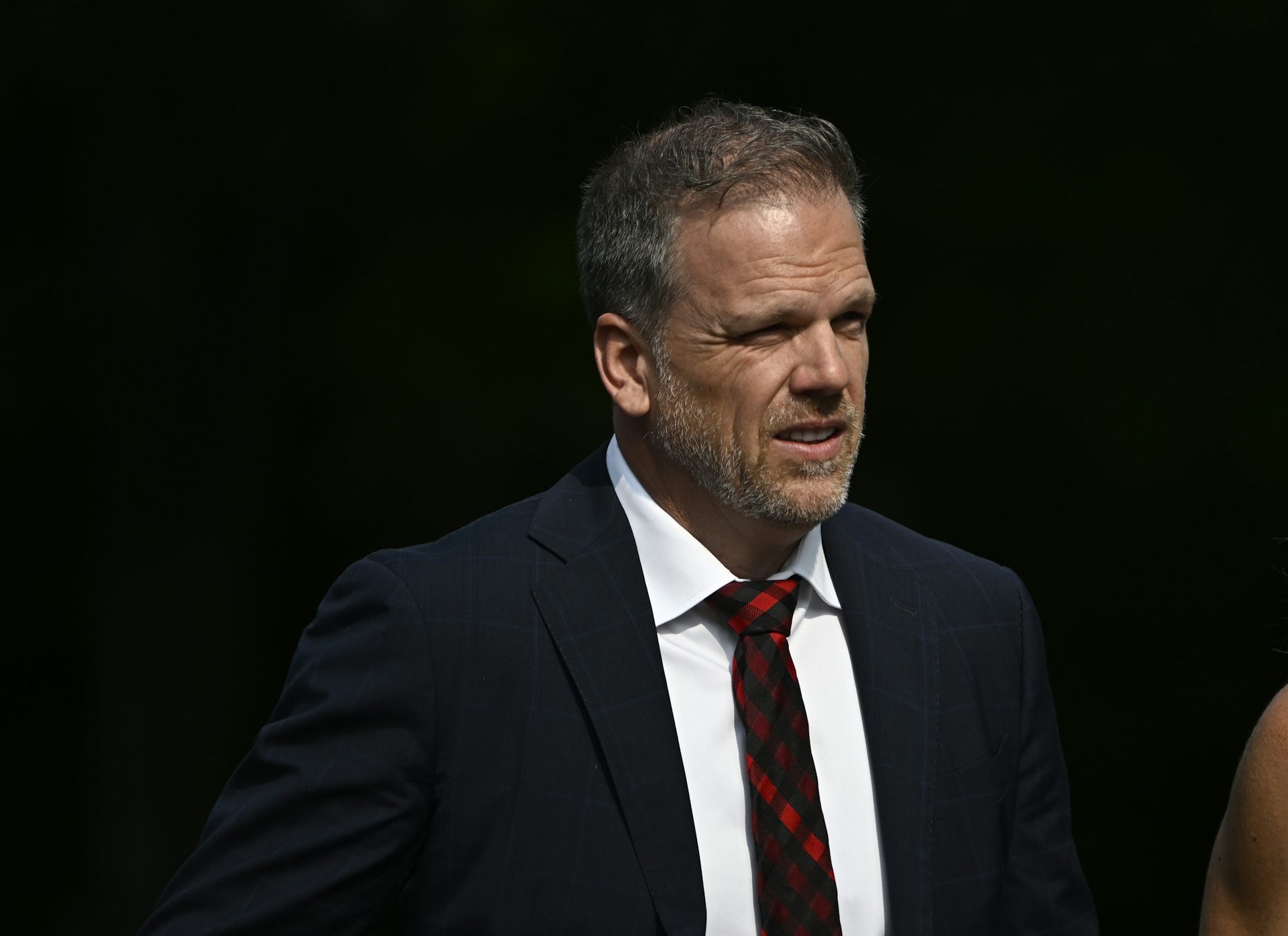 A man in a dark suit and tie against a dark background