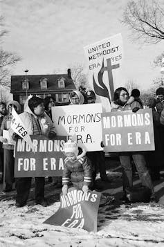 A black and white photo of around a dozen women holding signs at a protest in the snow.