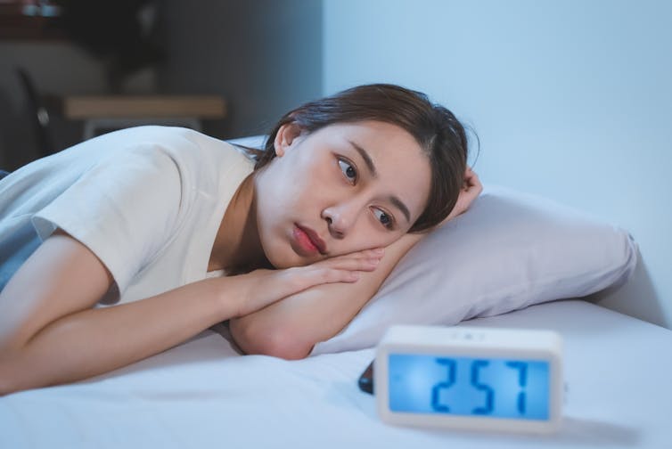 A woman lies in bed trying to sleep.