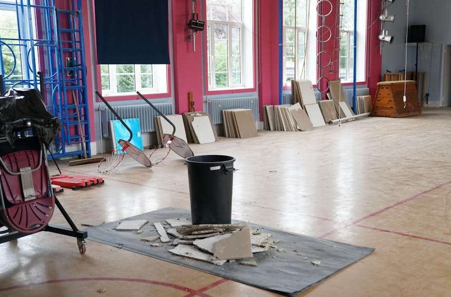 A large, empty room in a school with chunks of Raac ceiling that have collapsed onto the floor