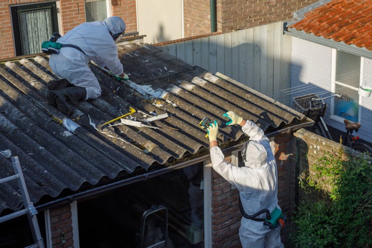 Workers in full body protection removing asbestos from a small structure with a corrugated metal roof