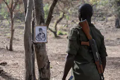 Man with gun looking at framed drawing pinned to tree