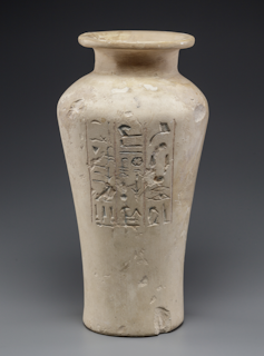 A white vase-shaped ceramic jar with hieroglyphics engraved on the side.