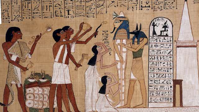 Egyptian art showing people waving objects at a sarcophagus. 