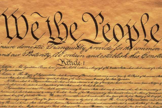 The phrase 'We the People' written on parchment paper above a lot of antique-looking writing.