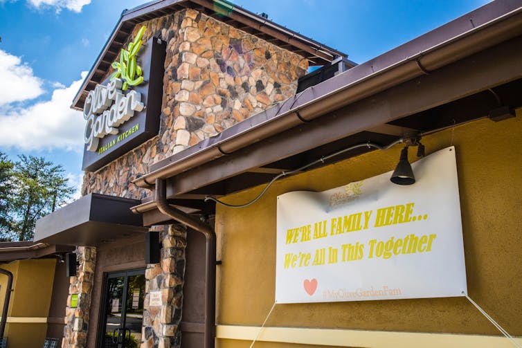 Outside shot of Olive Garden restaurant with a sign that says We're all family here ... we're all in this together.