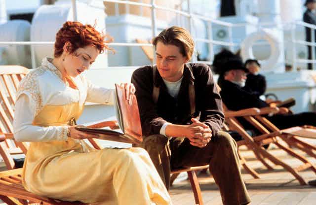 Film still of Kate Winslett (Rose) and Leonardo DiCaprio (Jack) on the Titanic, characters are sitting in deckchairs looking at a notebook.