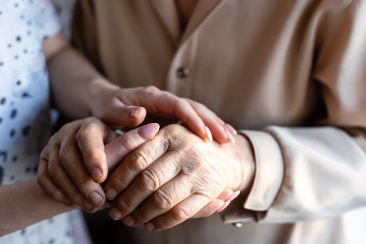 Close up of an elderly woman's hands being held by a younger woman.