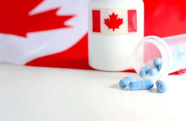 A bottle of blue capsules tipped over, beside a larger bottle with a Canadian flag label, and a Canadian flag in the background
