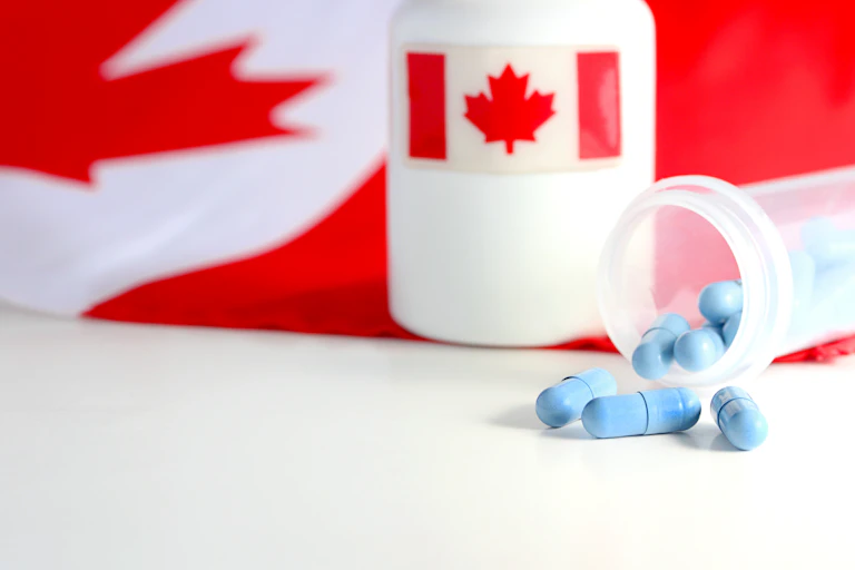 A bottle of blue capsules tipped over, beside a larger bottle with a Canadian flag label, and a Canadian flag in the background
