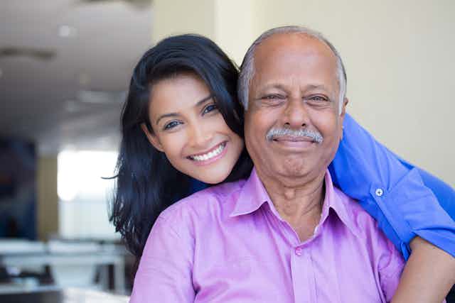 A young South Asian woman and older South Asian man pose for a photo.