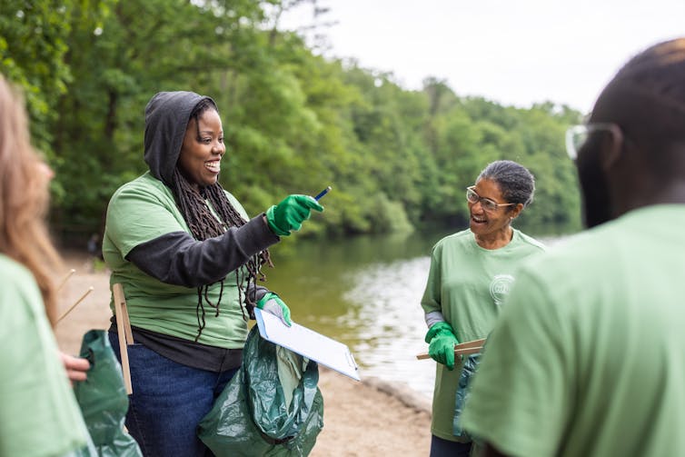 女性がゴミ袋を持ち、他の人たちを指導して湖岸の掃除をしている。