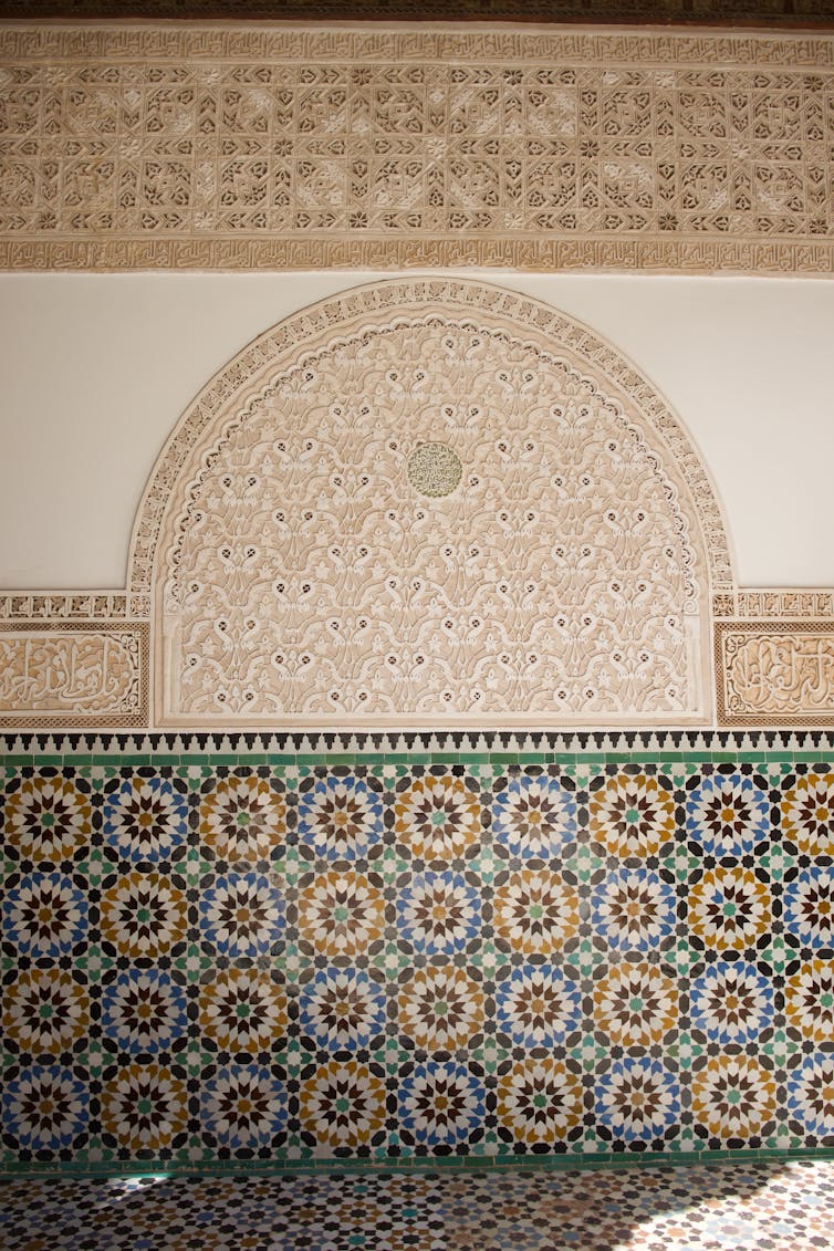 An wall with multicolored tiles and carved plaster decoration.