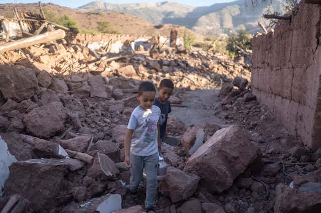 Two boys seen walking amid the rubble of a home.