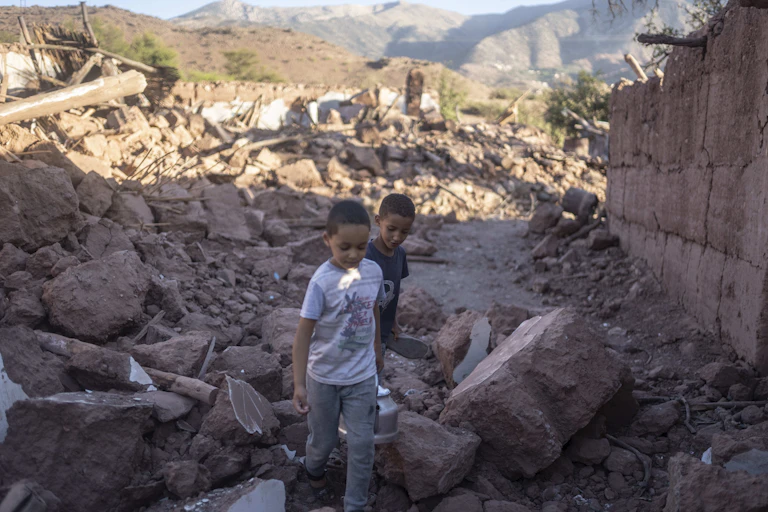 Two boys seen walking amid the rubble of a home.