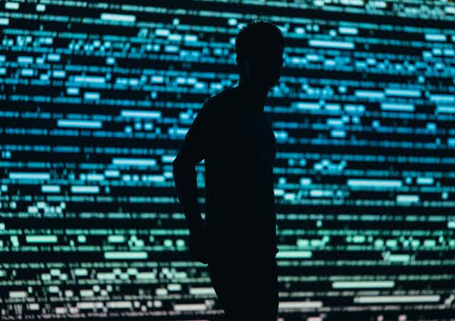 A silhouetted person against a blurry backdrop of what look like blue and green lines of code
