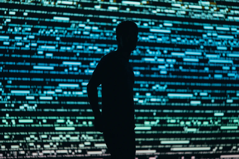 A silhouetted person against a blurry backdrop of what look like blue and green lines of code