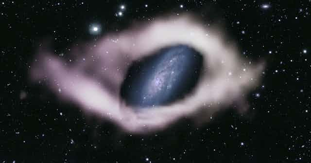 A photo showing a spiral galaxy surrounded by a pale, ghostly ring of gas.