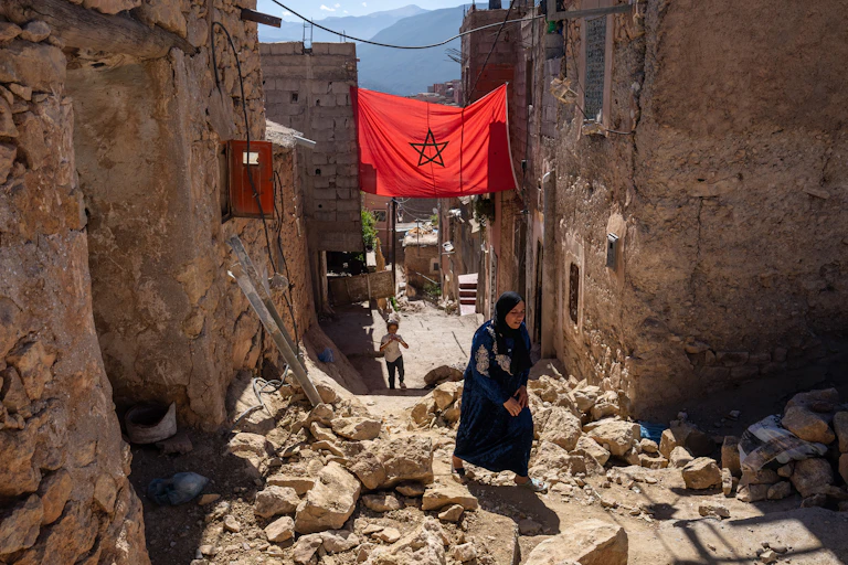 A woman walks past the rubble of damaged buildings