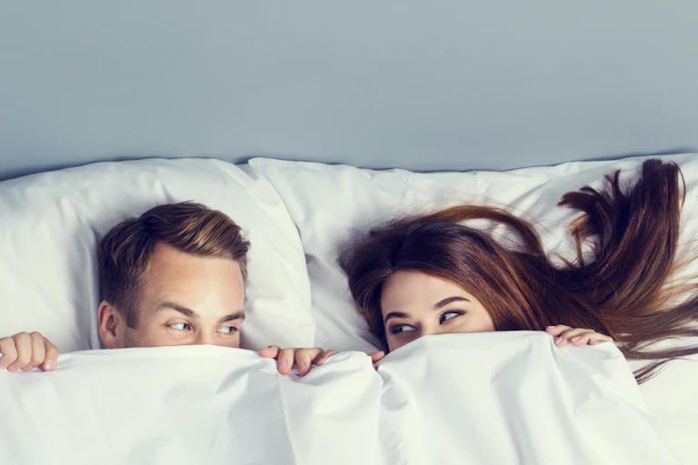 Young couple peeping from bedsheet on the bed at bedroom