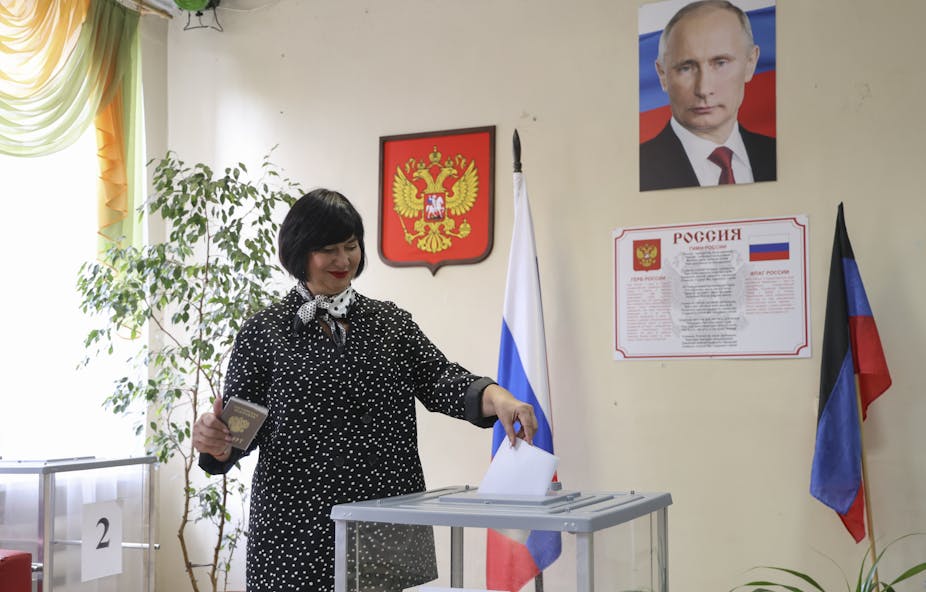 A woman casts her vote in an office in Donetsk, eastern Ukraine, under a poster of Vladimir Putin.