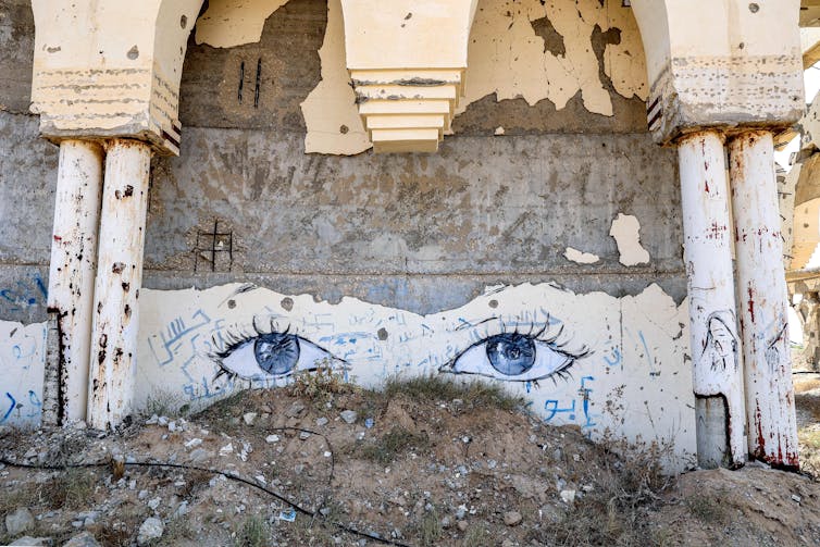 A mural of eyes painted on a crumbling wall.