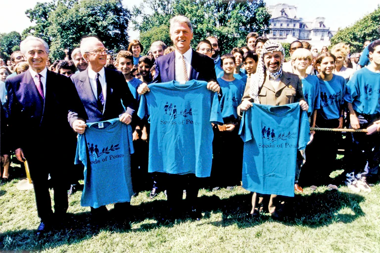 Shimon Peres, Yitzhak Rabin, Bill Clinton and Yasser Arafat, right, pose holding t-shirts that say seeds of peace.