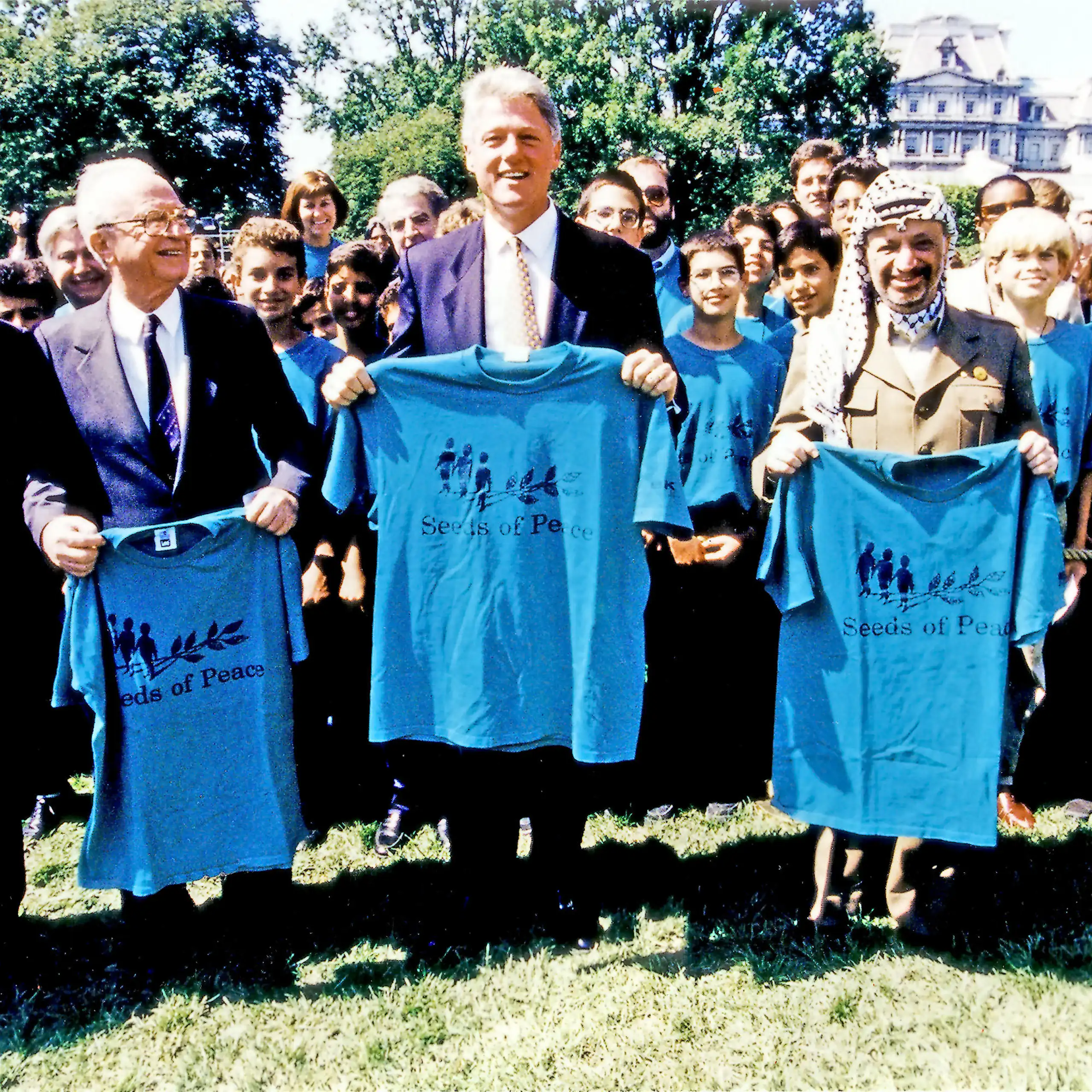 Shimon Peres, Yitzhak Rabin, Bill Clinton and Yasser Arafat, right, pose holding t-shirts that say seeds of peace.