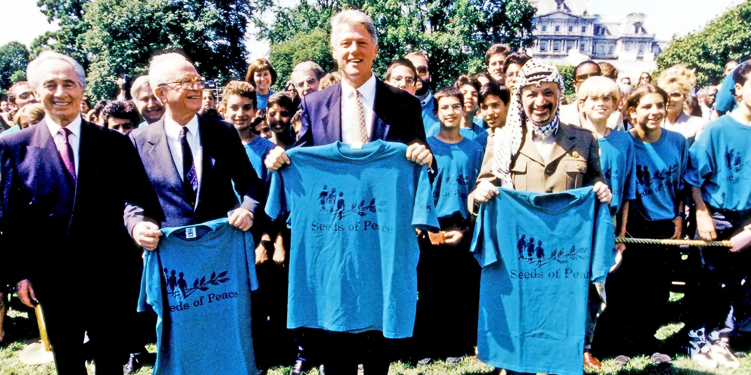 Shimon Peres, Yitzhak Rabin, Bill Clinton and Yasser Arafat, right, pose holding t-shirts that say seeds of peace. 
