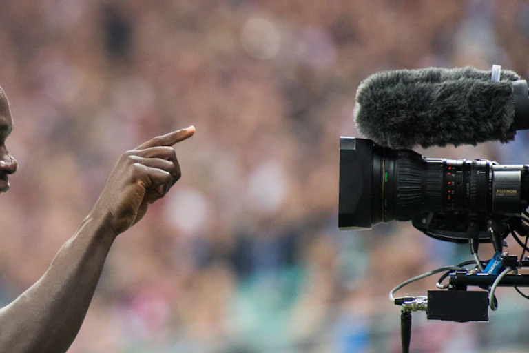 A man, sweating from exertion in a stadium full of people points a finger directly at a television camera