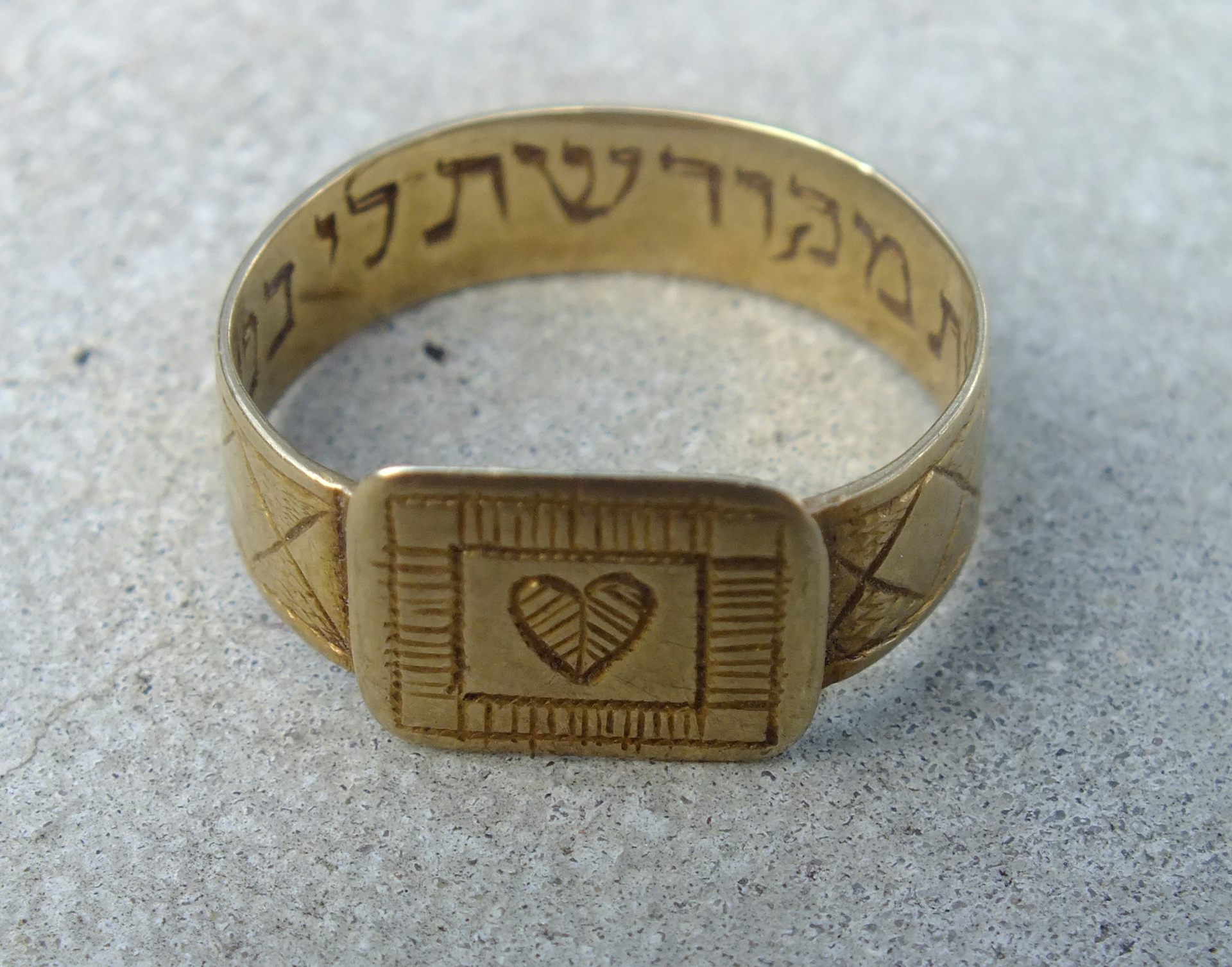 A gold wedding band engraved with a heart and Hebrew writing.