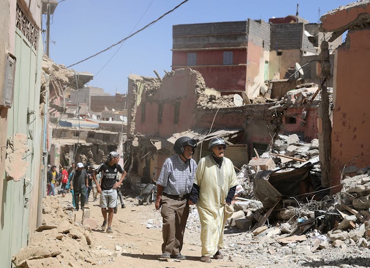 A group of people walk by buildings devastated by the earthquake.