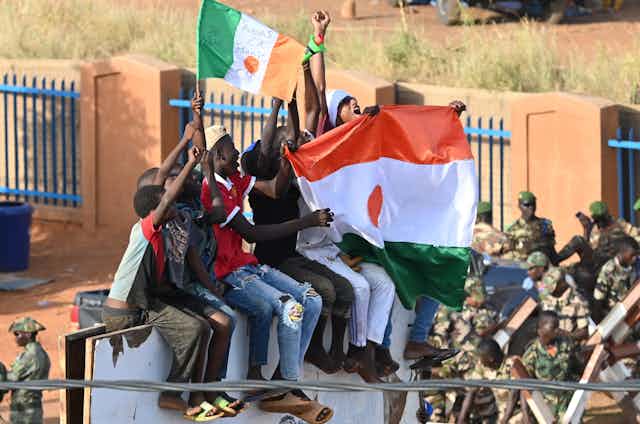A group sit on a structure holding aloft Niger flags.