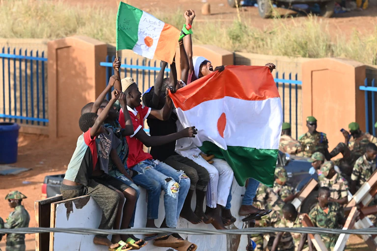A group sit on a structure holding aloft Niger flags.