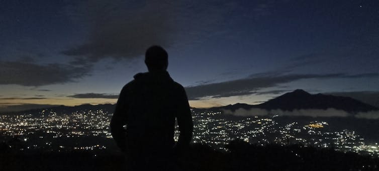 person silhouetted against a sunrise over a distant cityscape