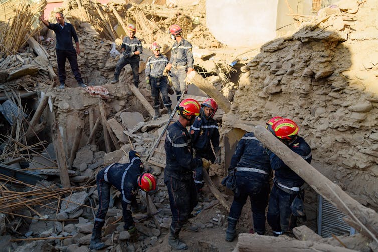 Amidst the rubble, a team of uniformed firefighters in hard hats search through the debris left by the quake.