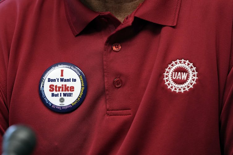 Closeup of a red polo shirt with a UAW logo on one side and a button on the other saying 'I don't want to strike but I will!'