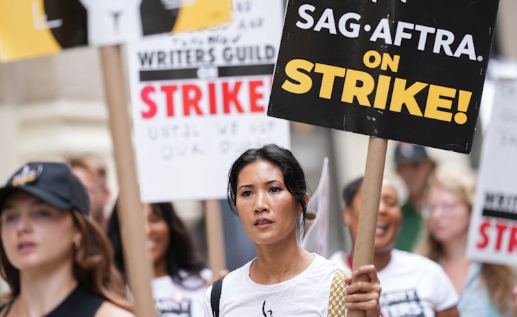 Women on a picket line holding signs saying that the Writer's Guild and SAG AFTRA unions are on strike.