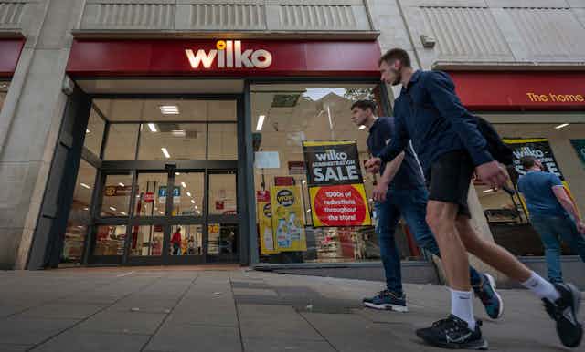 Three men walk past a Wilko shopfront with a sign advertising 1000s of reductions in its administration sale.