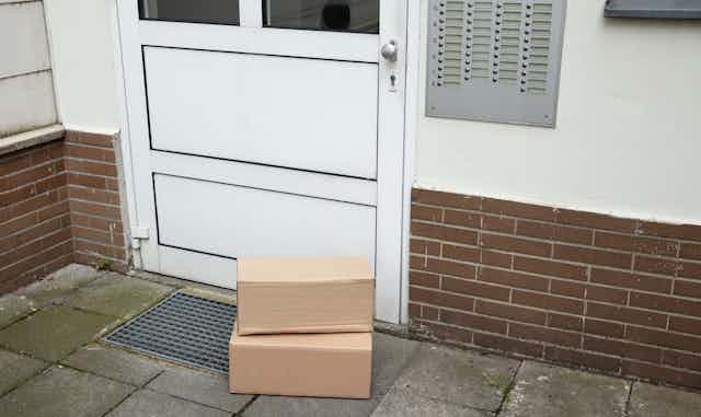 Two unmarked packages stacked up in front of a door on a dingy patio.