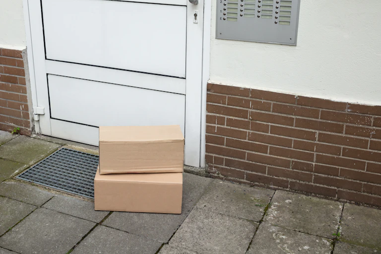 Two unmarked packages stacked up in front of a door on a dingy patio.