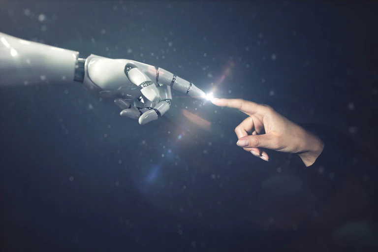 A white robotic hand's forefinger meets a human hand forehfinger, against a dark backdrop with speckles of light.
