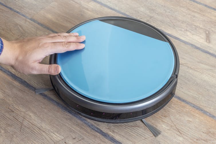 A hand petting a light blue, circular Roomba vacuum.